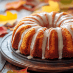 A cozy autumn-themed setting featuring a moist pumpkin olive oil cake with a shiny glaze drizzled on top, surrounded by vibrant fall leaves in warm hues of orange and red